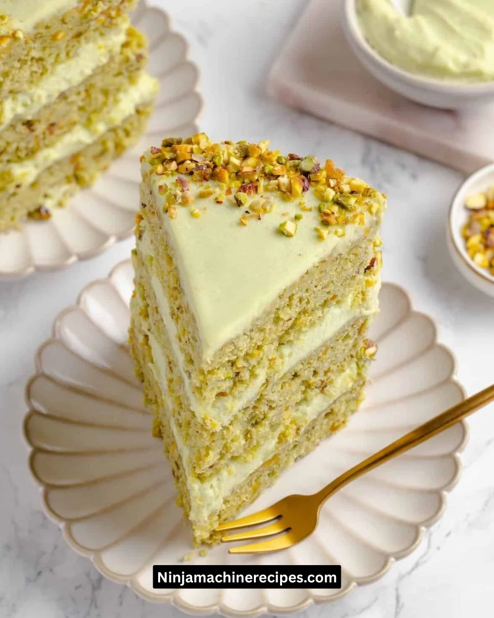 A slice of moist Pistachio Cake topped with crushed pistachios and cream frosting.