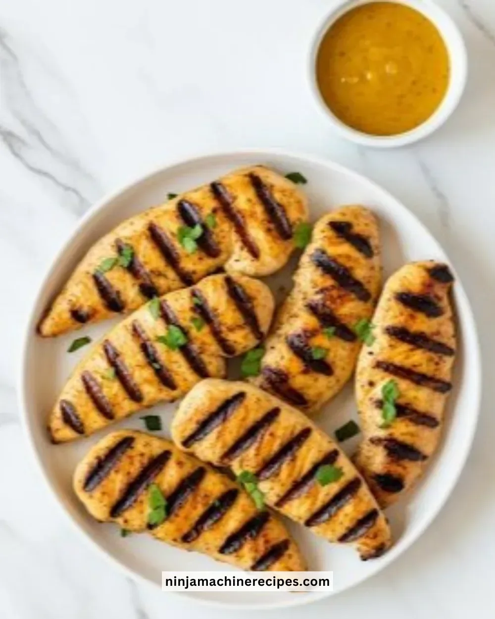 Juicy grilled chicken tenders served on a plate with fresh herbs.