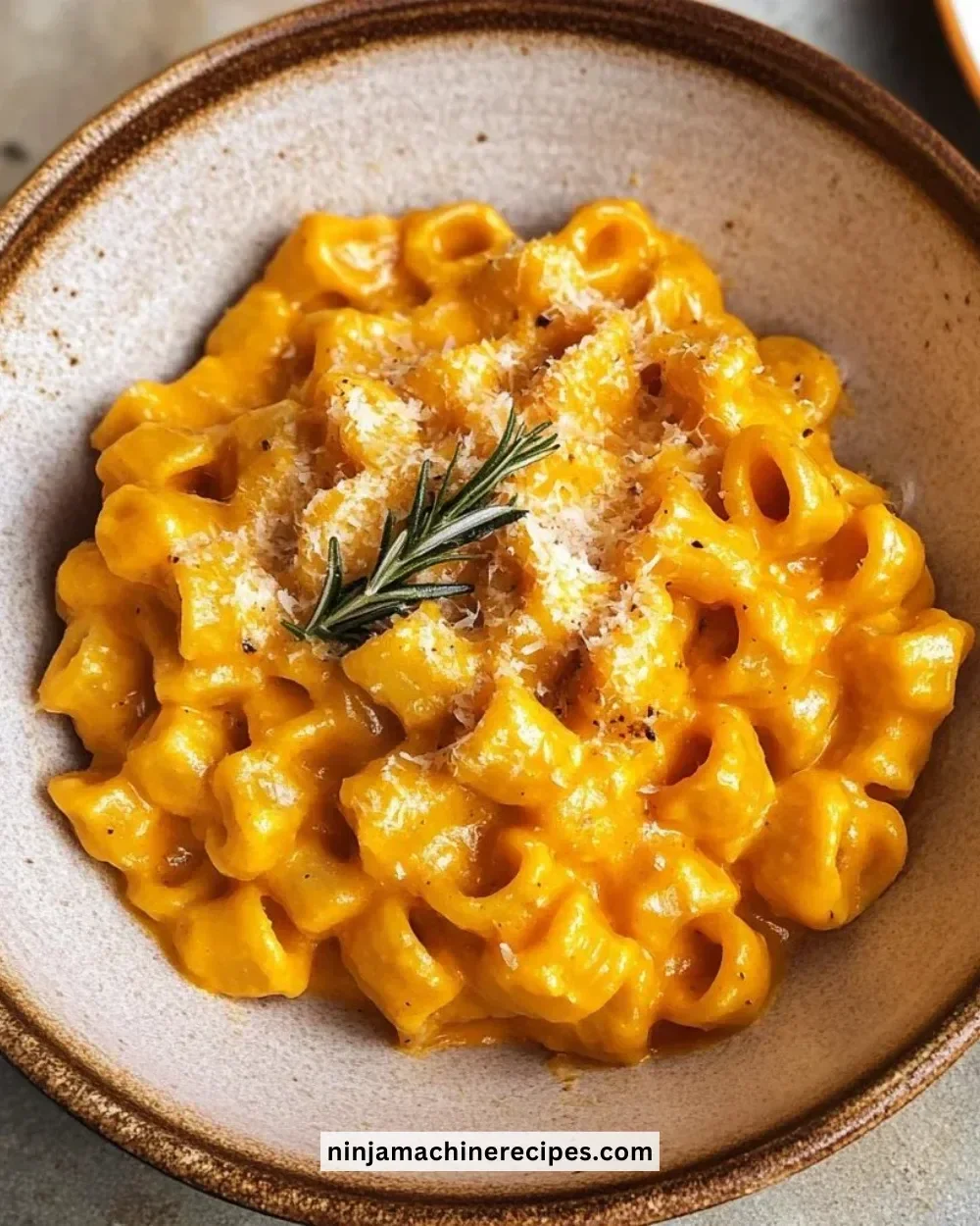 Bowl of roasted pumpkin and garlic pasta garnished with herbs