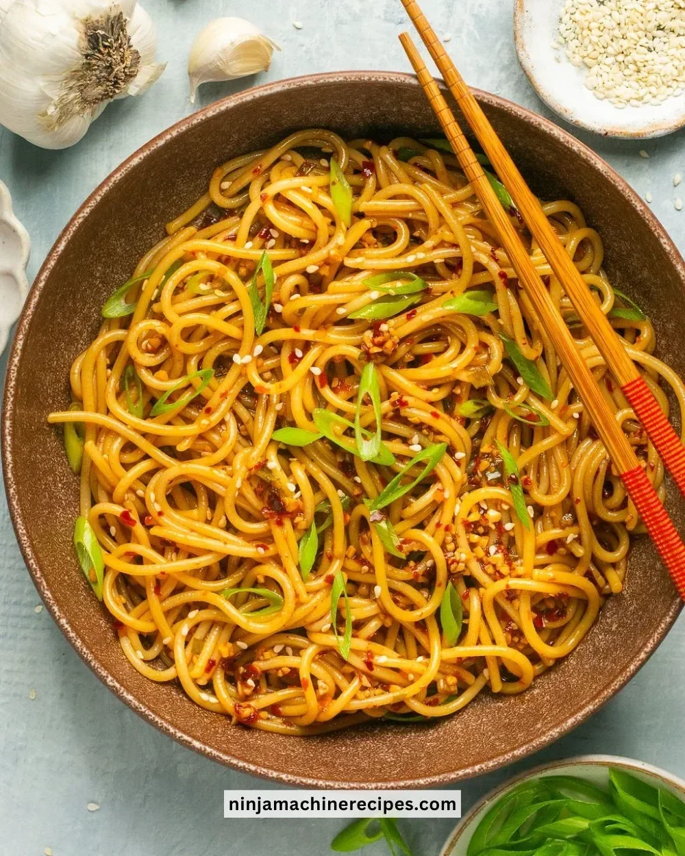Bowl of garlic chili oil noodles topped with fresh herbs and chili flakes.