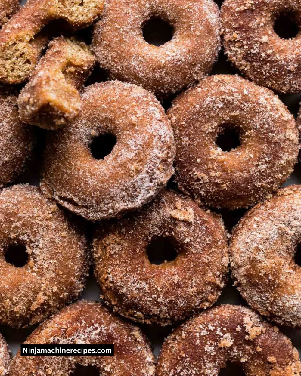 Baked apple cider donuts arranged on a wooden platter with cinnamon sticks.