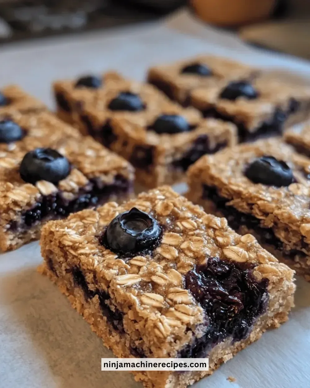 Baked oatmeal blueberry bars on a wooden cutting board, topped with fresh blueberries.
