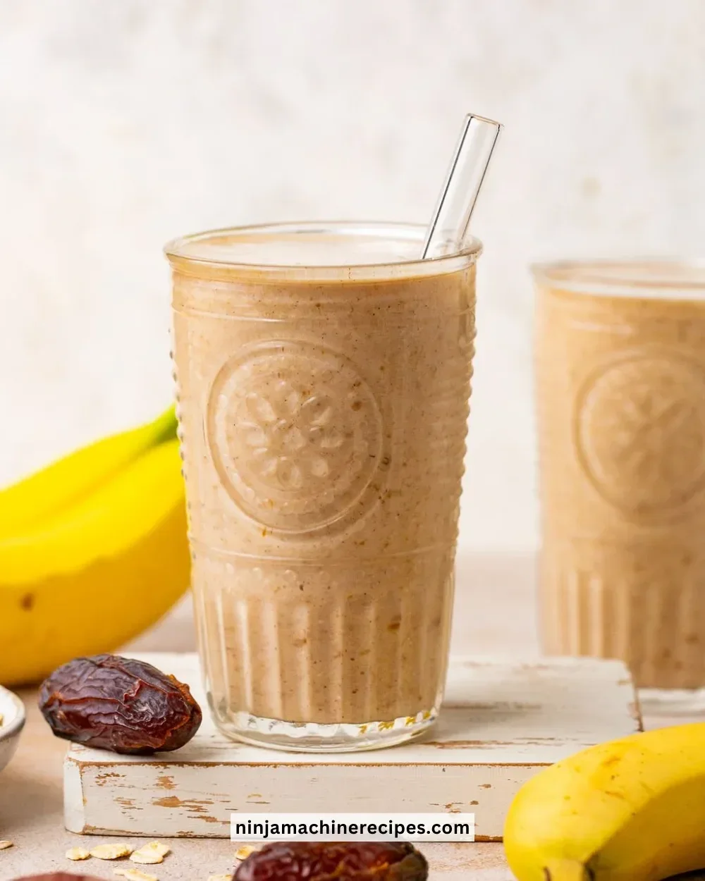 A refreshing Banana Date Smoothie in a glass, topped with banana slices and dates.