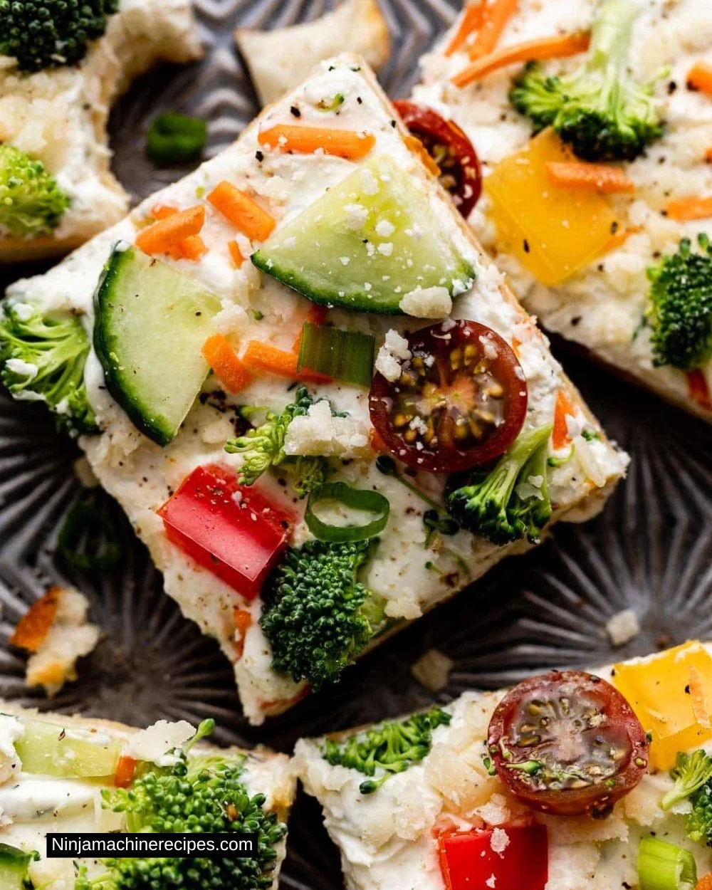 Slice of cold veggie pizza topped with fresh vegetables and herbs.