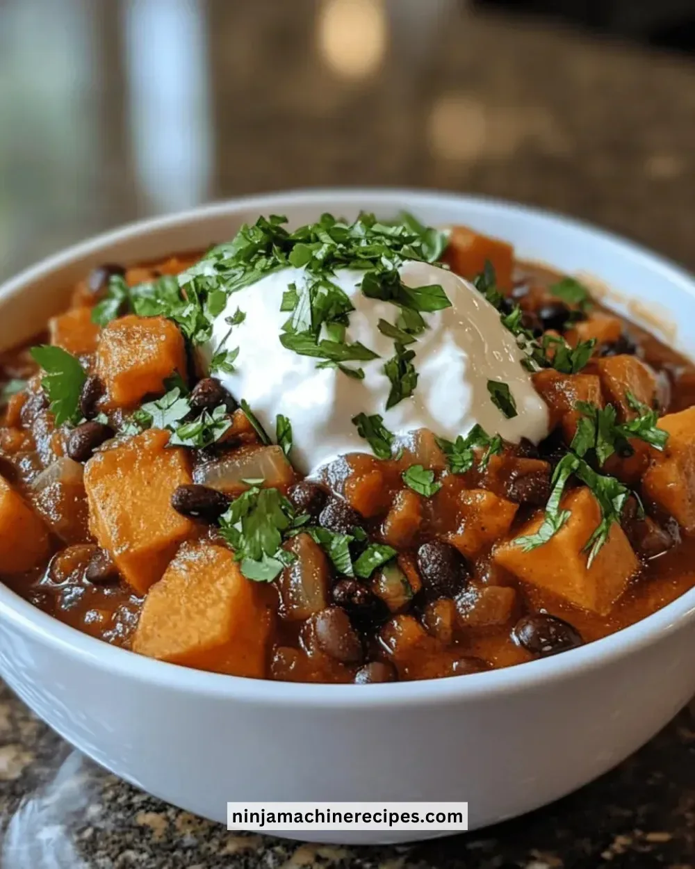 Bowl of sweet potato black bean chili topped with fresh herbs and avocado