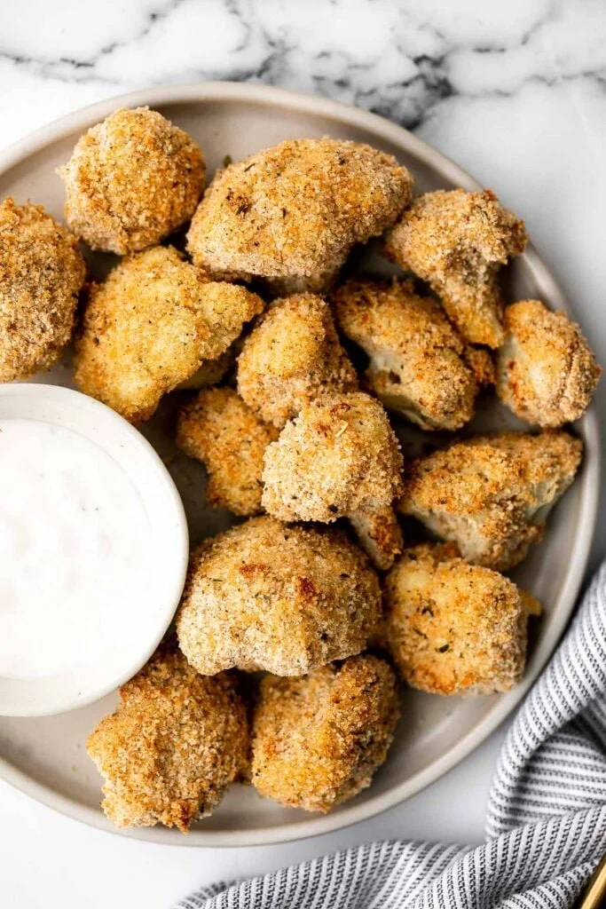 Baked cauliflower nuggets served on a plate with a dipping sauce.
