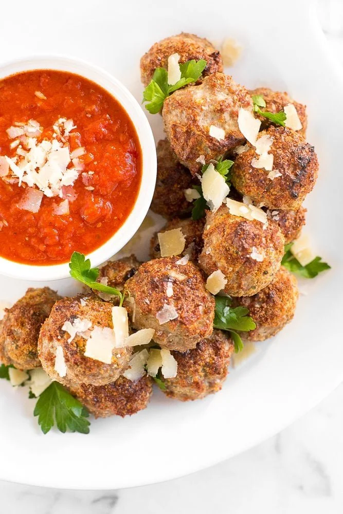 Baked turkey meatballs served on a plate with fresh herbs and sauce.