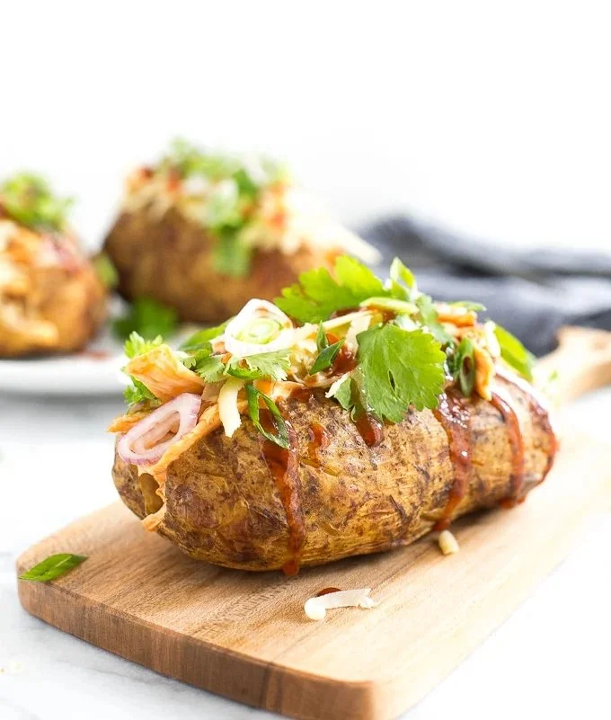 BBQ chicken stuffed baked potatoes garnished with green onions on a plate.