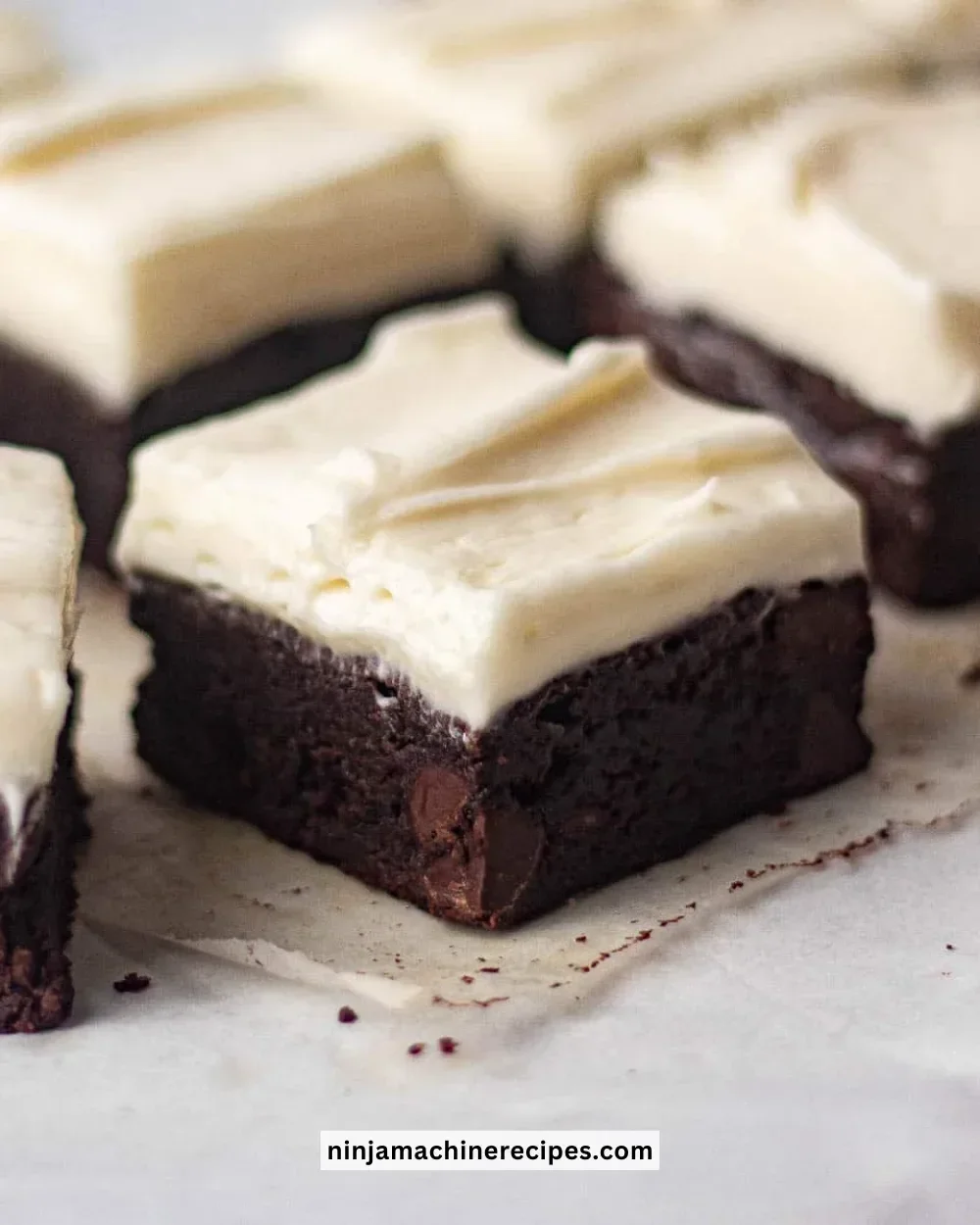 Delicious brownies with creamy cream cheese frosting on a white plate.
