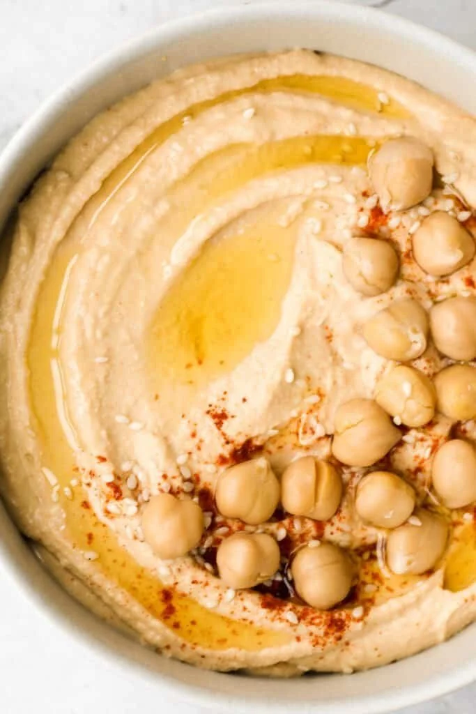 Bowl of creamy classic hummus garnished with olive oil and parsley