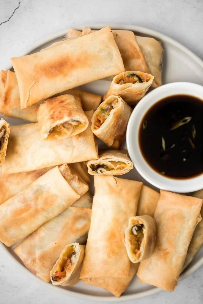 Plate of crispy fried vegetarian spring rolls served with dipping sauce.