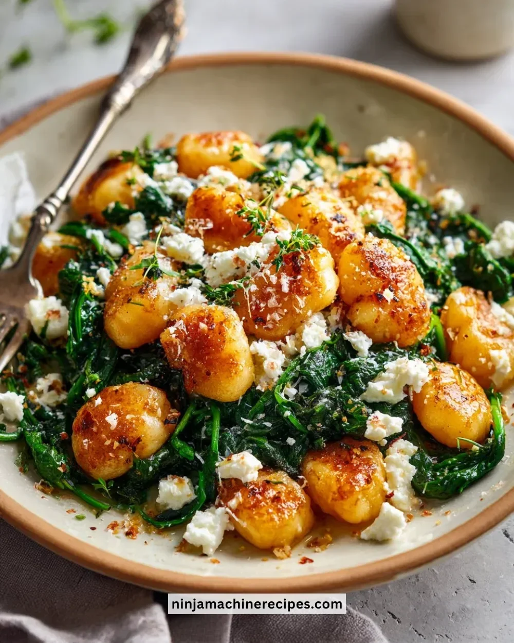 Crispy gnocchi with sautéed spinach and crumbled feta cheese on a plate.