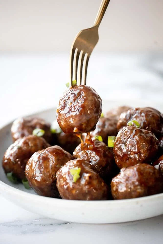 Plate of sticky honey garlic meatballs garnished with sesame seeds and green onions