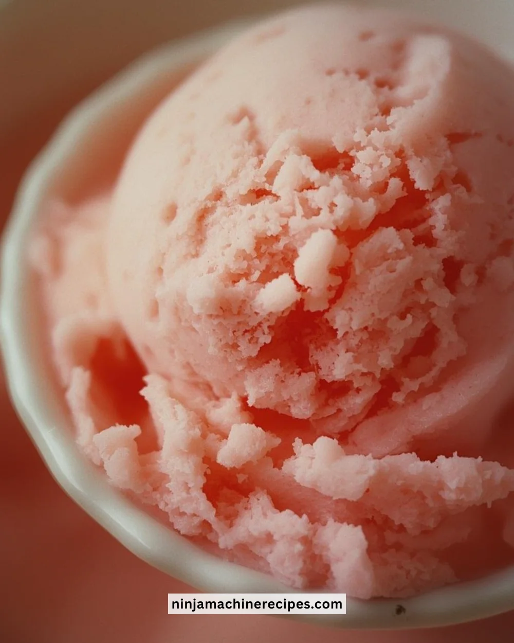 Bowl of creamy strawberry ice cream topped with fresh strawberries.
