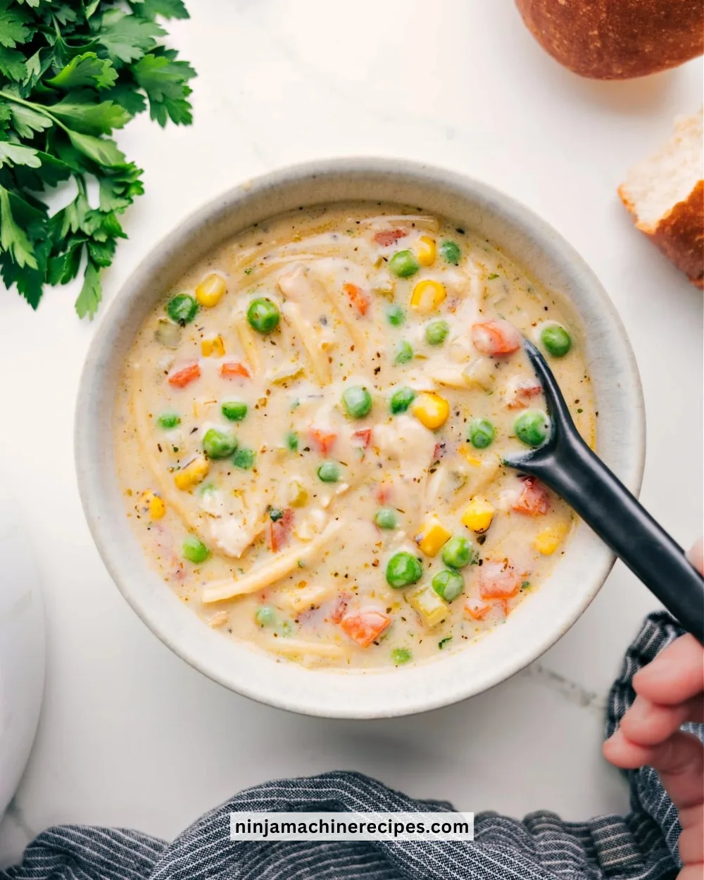 A bowl of creamy chicken soup garnished with herbs and vegetables.