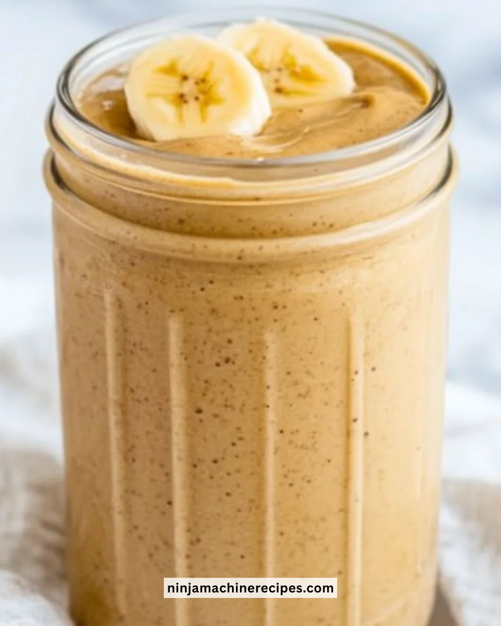 A creamy Peanut Butter Banana Smoothie in a glass with a banana and peanut butter on the side.