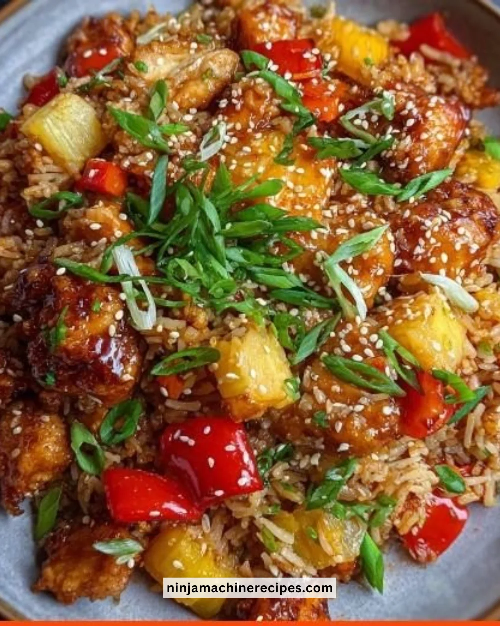 Bowl of sweet and sour chicken fried rice with colorful vegetables and chicken pieces.