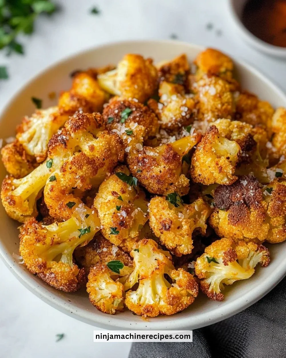 Crispy roasted cauliflower served in a bowl, garnished with herbs.