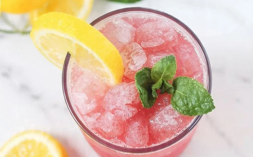 A refreshing pink lemonade slushie in a glass with ice and a lemon slice.