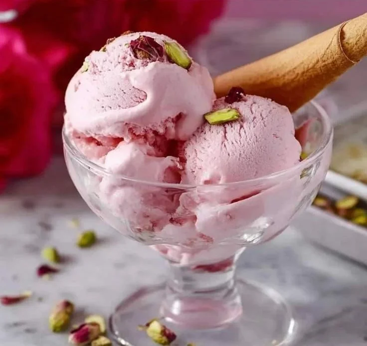 A creamy bowl of rose ice cream garnished with rose petals and nuts