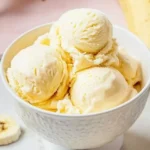 A bowl of creamy banana pudding ice cream topped with whipped cream and banana slices.