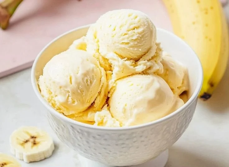 A bowl of creamy banana pudding ice cream topped with whipped cream and banana slices.