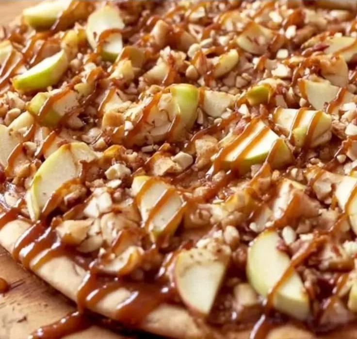 A slice of caramel apple dessert pizza topped with caramel and apple slices.