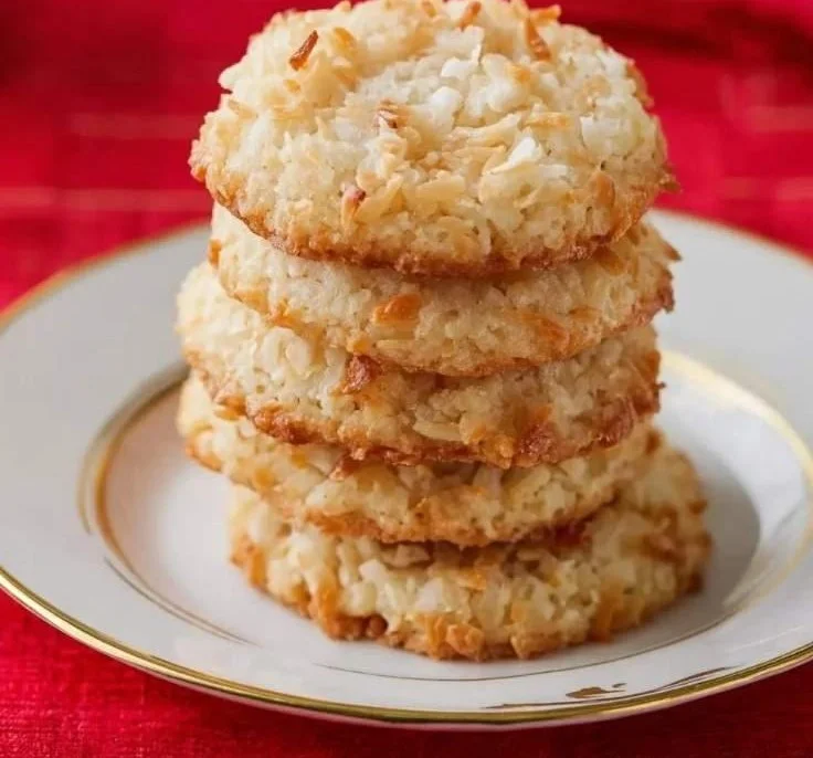 Delicious coconut cookies on a wooden plate with coconut flakes on top.