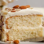 Sliced creamy almond cake decorated with almonds on a white plate
